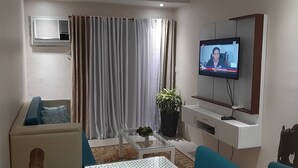 A living room with a sofa, a TV, a potted plant, and a window with curtains. - Affordable Luxury 2BR Condo in Davao City (Davao City)