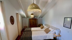 Hotelkamer met twee bedden, een geweven lamp, een houten garderobe, een kleine ronde tafel en een aan de muur hangend schilderij.