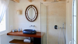 Een badkamer met een houten wastafelmeubel, een ronde spiegel, een douche met een handdouche en een getextureerd vloerkleed.