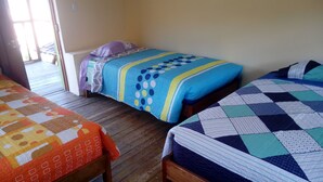 A room with two beds, each with a distinct quilt pattern. The room has wooden flooring and a door leading outside. - ewwwwwwwww (Cusco)