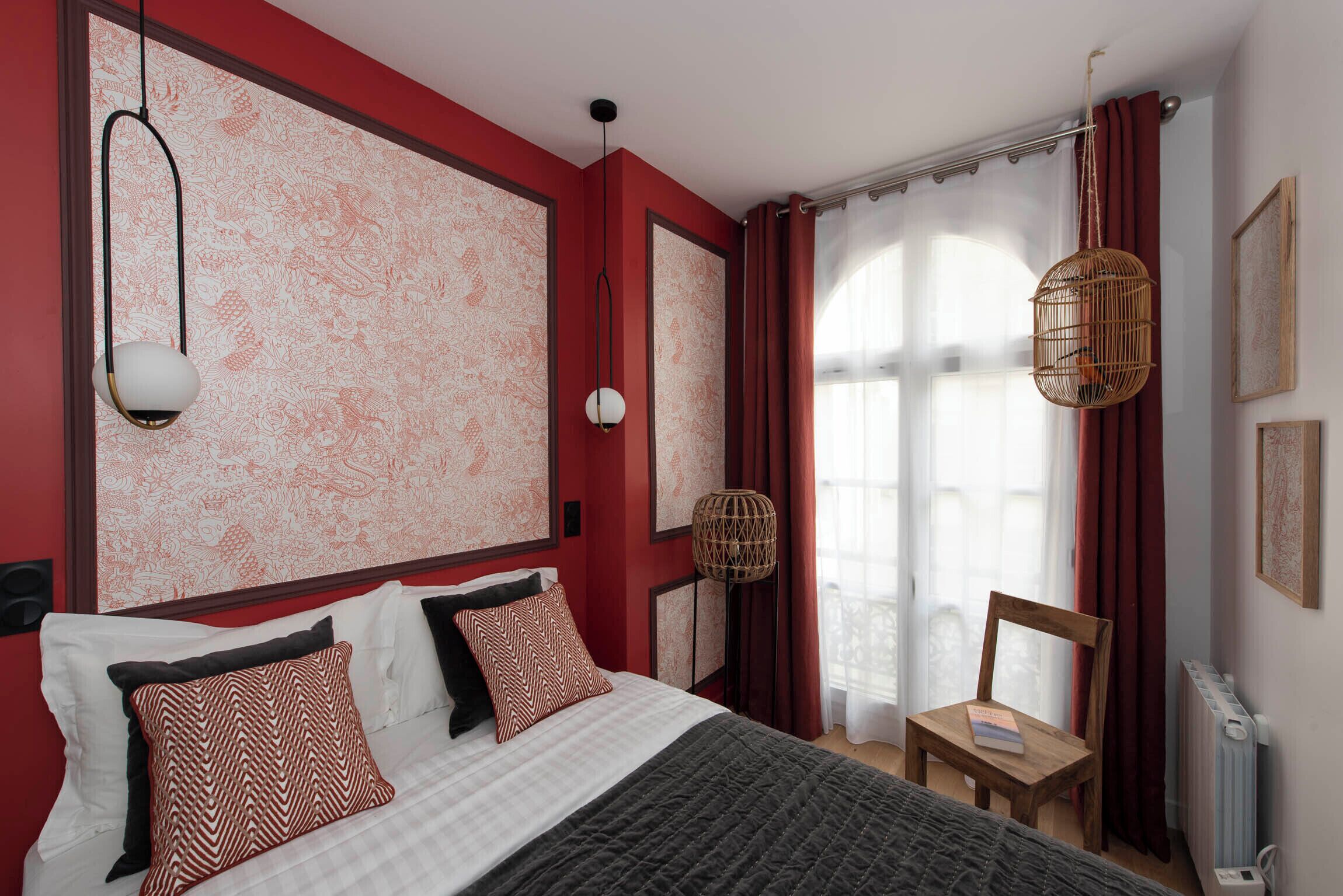 A bedroom with a large bed, a chair, a hanging light fixture, and a window with curtains.