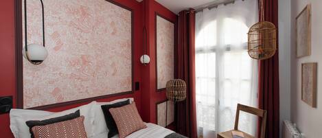 A bedroom with a large bed, a chair, a hanging light fixture, and a window with curtains.