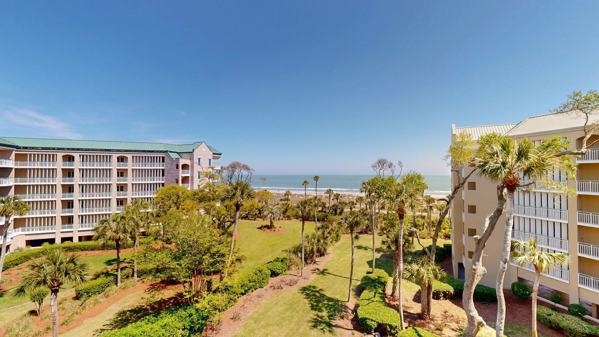 A hotel with multiple floors, a well-maintained lawn, and a view of the beach.