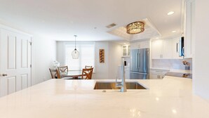 Une cuisine moderne dotée d’un îlot central, d’appareils électroménagers en acier inoxydable et d’un coin repas avec des chaises en bois.