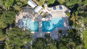 Vue aérienne d’une propriété dotée de deux piscines, d’un patio couvert et d’une végétation luxuriante.