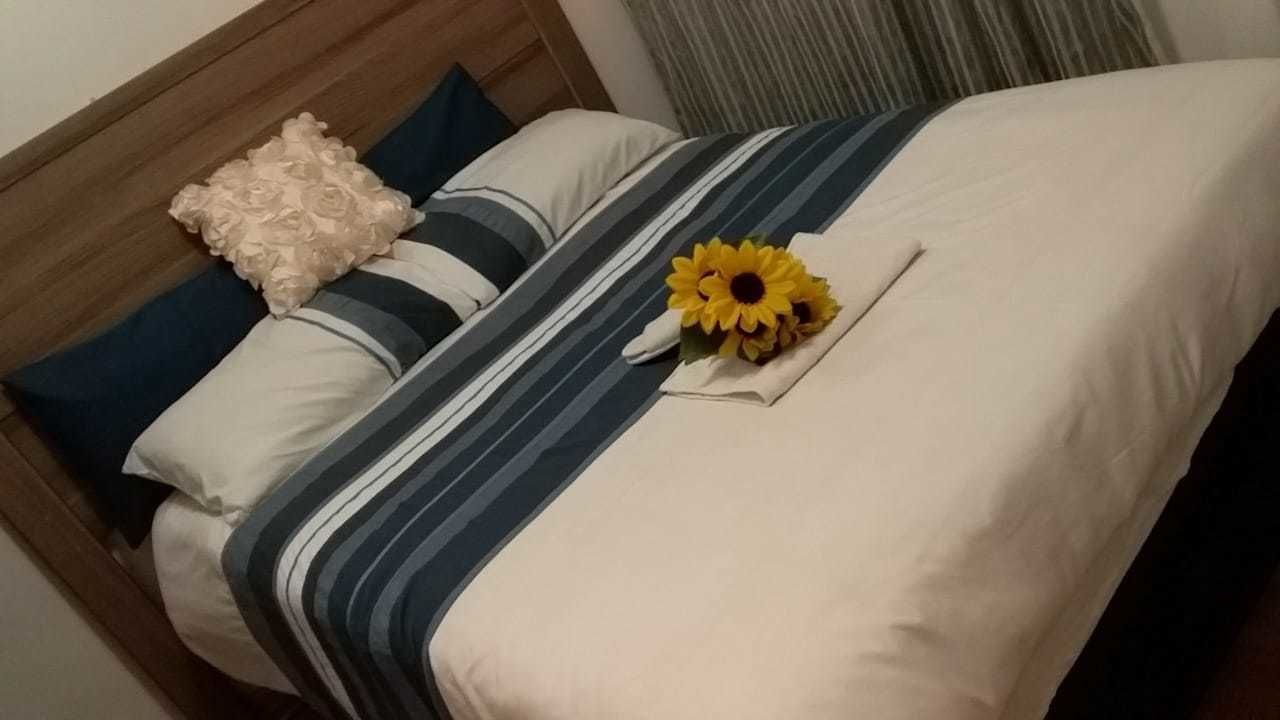 A neatly made bed with a striped bedspread, a decorative pillow, and a sunflower arrangement.