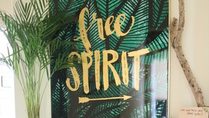 A room with a wooden console table displaying a 'Free Spirit' poster, a potted plant, a lantern, and a welcome sign.
