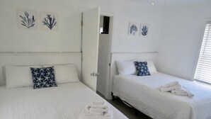 A hotel room with two beds, each with a white bedspread and a single pillow. There are towels neatly folded on each bed. - Saltaire Cottages 6: 2BR Steps to Private Beach Access Screen Porch Pool (Kitty Hawk)