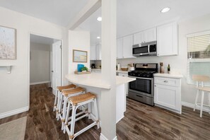 A modern kitchen with white cabinetry, a built-in microwave, and an oven. There are bar stools and a small island with a sink.