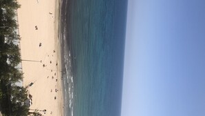 En strand med mennesker, der går langs kysten, og en klar himmel.