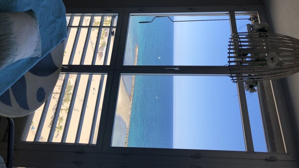 Et værelse med stort vindue med udsigt over en strand.