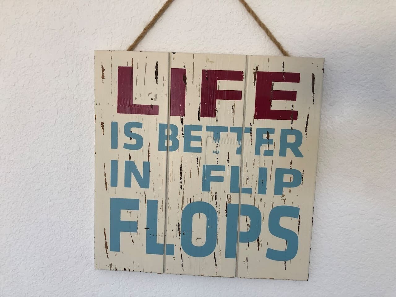 A sign with the text "LIFE IS BETTER IN FLIP FLOPS" on a wooden background.