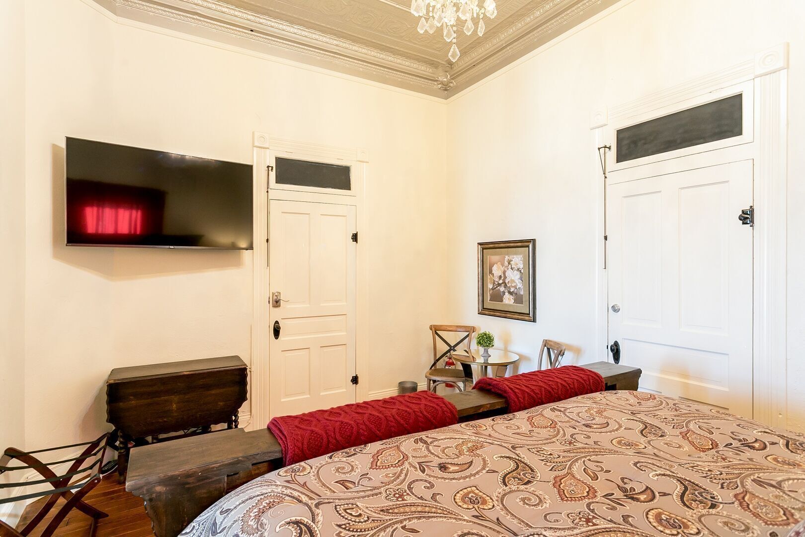 Une chambre à coucher avec un grand lit, un téléviseur fixé au mur, une porte et une petite table avec des chaises.