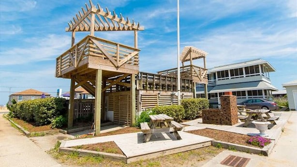 A wooden gazebo with a flagpole, picnic tables, and a building in the background. - Saltaire Cottages 5: 2BR Steps to Private Beach Access Screen Porch Pool (Kitty Hawk)
