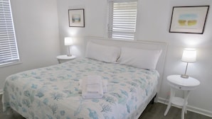 A bedroom with a bed, two bedside tables, and a window with blinds. - Saltaire Cottages 5: 2BR Steps to Private Beach Access Screen Porch Pool (Kitty Hawk)