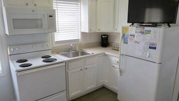 A compact kitchen with white cabinets, a microwave, stove, sink, and a refrigerator.