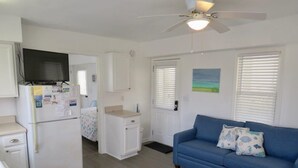 A compact living space with a kitchenette, a blue sofa with decorative pillows, and a ceiling fan.