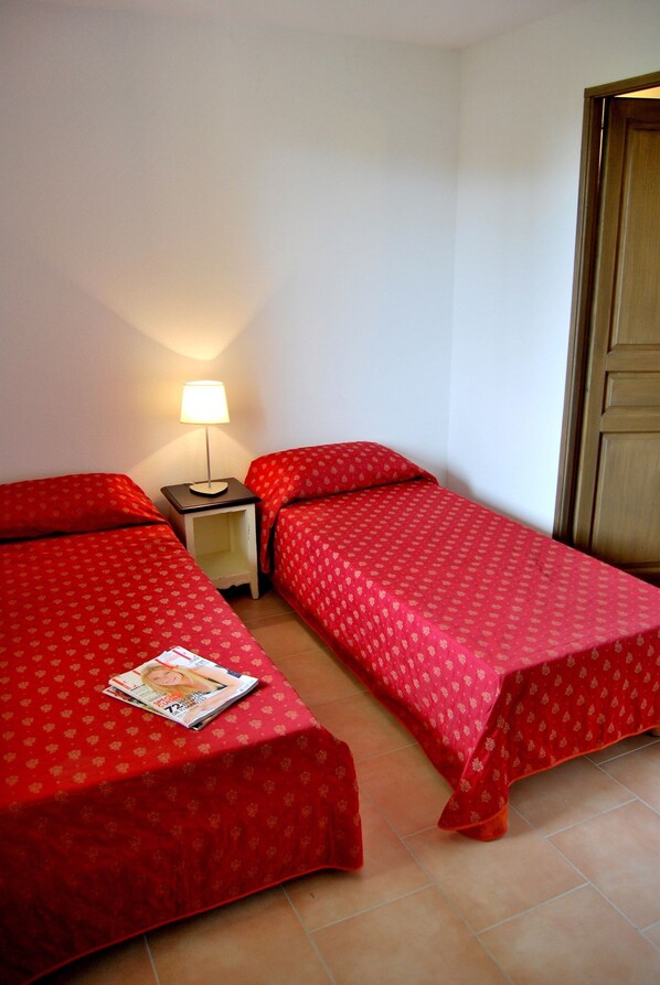 Une petite pièce avec deux lits simples, une table de chevet avec une lampe et une porte en bois.