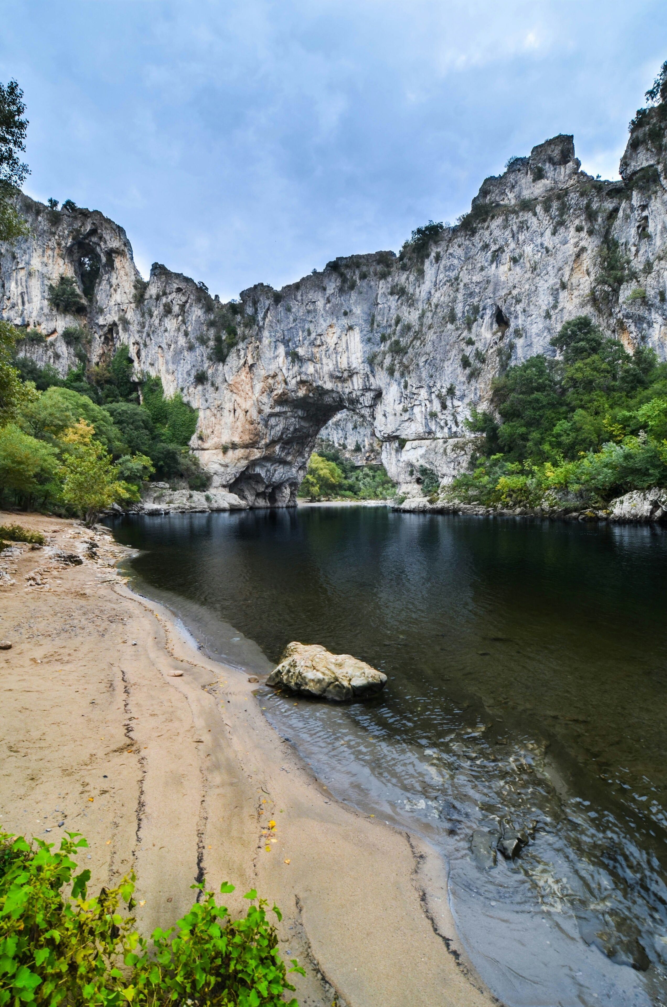 Un paisaje natural con un río, una playa de arena y acantilados rocosos.