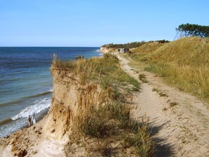 Ein Küstenpfad mit einem sandigen Weg, der zu einer Klippe mit Blick auf das Meer führt.