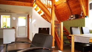 A spacious room with a wooden ceiling, a dining table with chairs, a black chair, and a staircase leading to another level. - House Dina Ahrenshoop (Ahrenshoop)