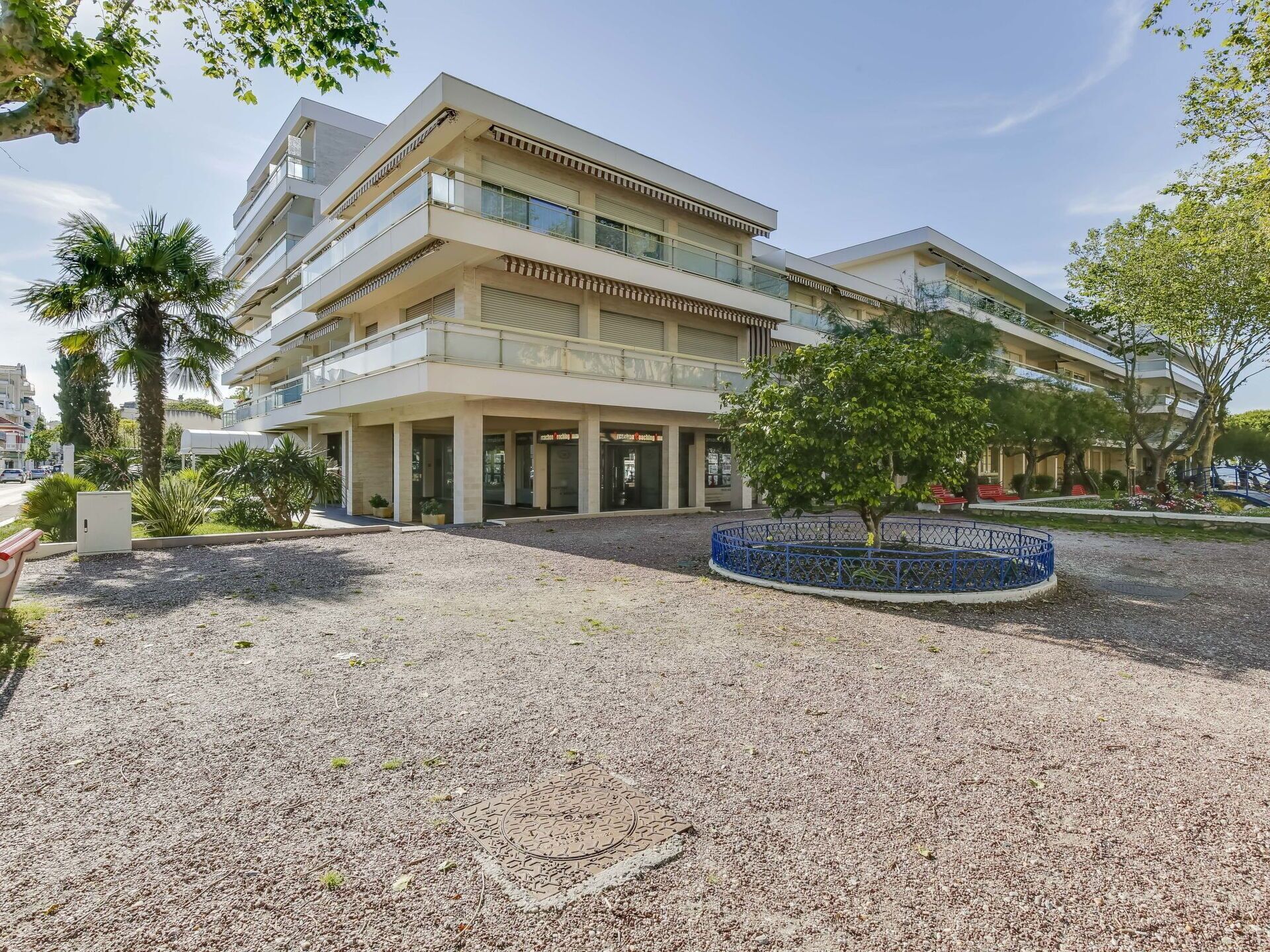Ein mehrstöckiges Hotel mit Innenhof, Gartenmöbeln und einem blauen Zierzaun.
