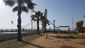 Un parc côtier doté d’un pont, de palmiers, de balançoires et d’une piste cyclable.