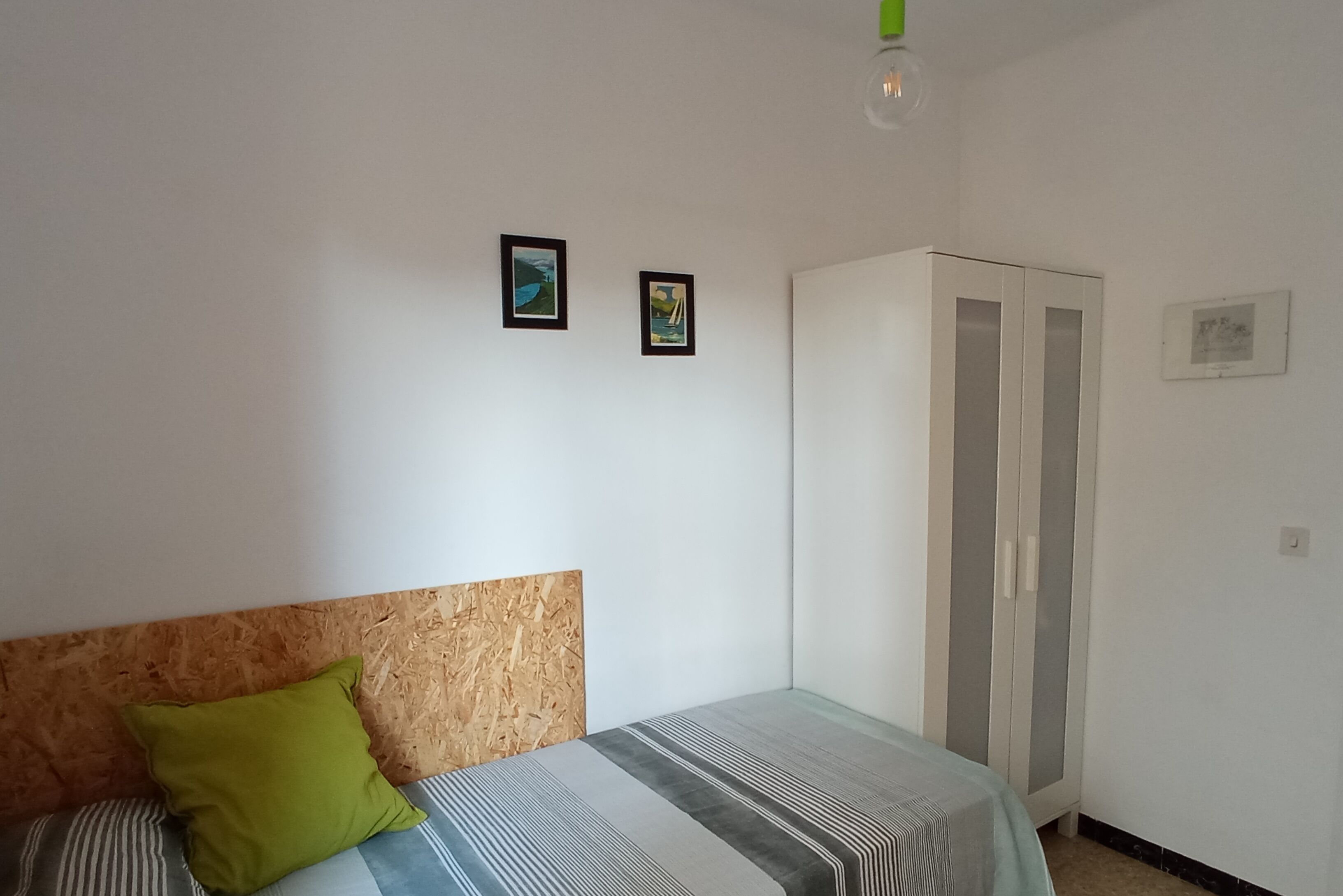 A bedroom with a bed, a green pillow, a wardrobe, and two framed pictures on the wall.