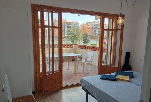 A room with a bed, a guitar, and a balcony with a table and chairs.