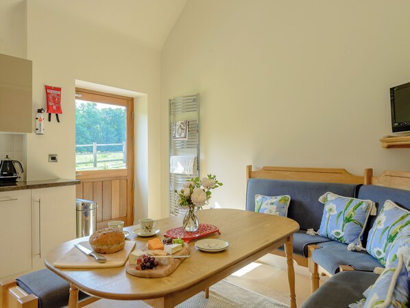 A cozy room with a wooden table set for a meal, a sofa with floral cushions, and a TV mounted on the wall. - 1 bedroom accommodation in Rufford, near Newark (Rufford, near Newark)
