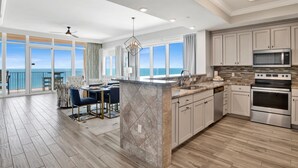 A modern kitchen with a large island, stainless steel appliances, and a view of the ocean. - Phoenix Orange Beach 1201 | Orange Beach, AL (Orange Beach)