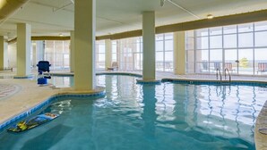 An indoor swimming pool with clear water, large windows, and lounge chairs. - Phoenix Orange Beach 1201 | Orange Beach, AL (Orange Beach)