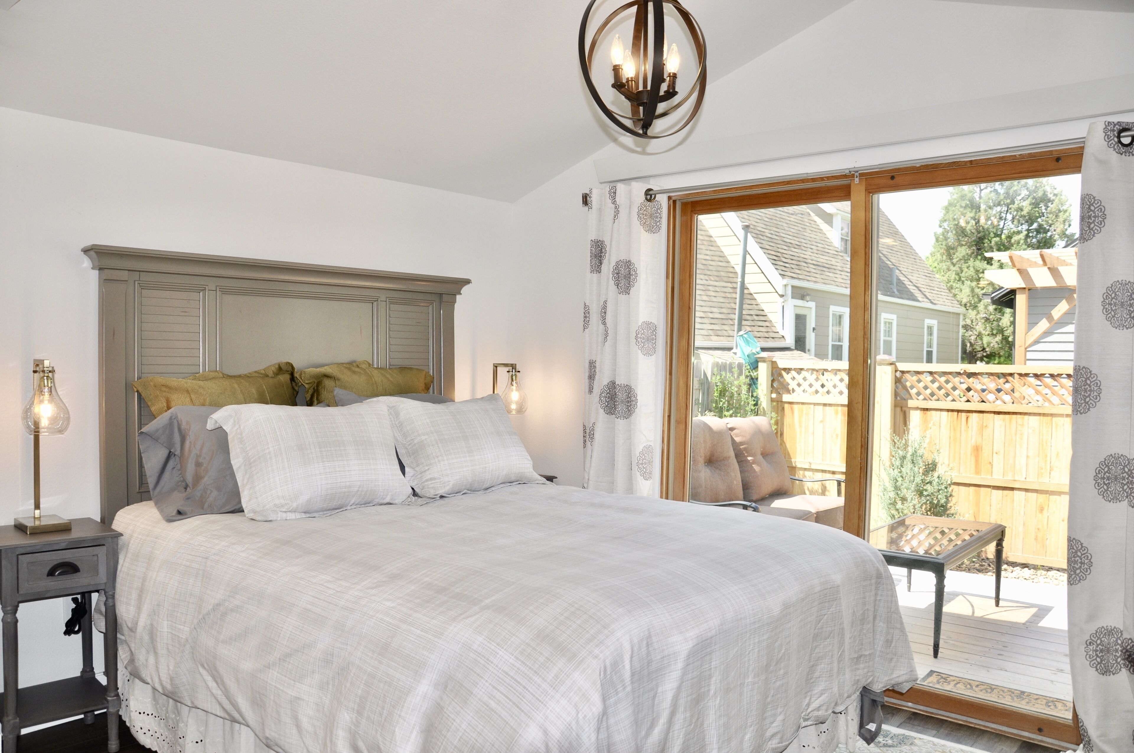 Ein Schlafzimmer mit einem großen Bett, einem Nachttisch mit Lampe, einem Holzkopfschild und Blick auf den Garten durch eine Schiebetür.
