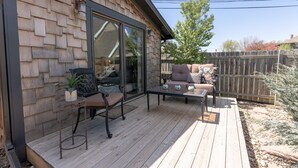 A wooden deck with outdoor furniture, a glass door leading to a covered area, and a wooden fence in the background.