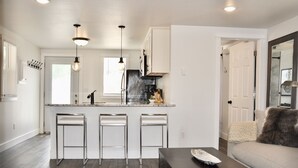 A modern kitchen with a central island, bar stools, pendant lighting, and a wooden coffee table.