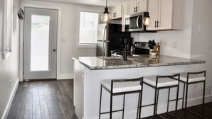 A modern kitchen with white cabinets, a large island with bar stools, stainless steel appliances, and pendant lighting.