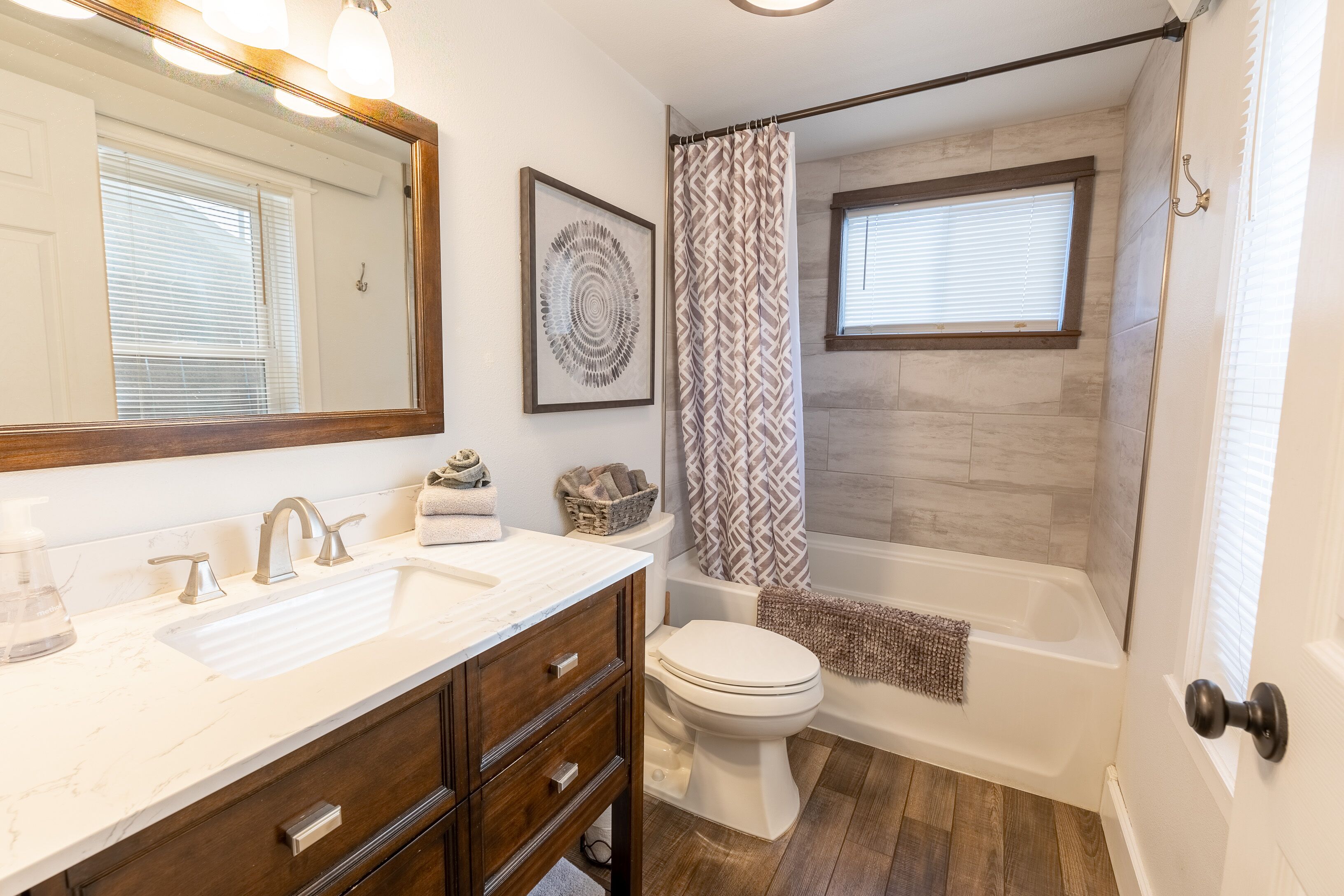 A bathroom with a white sink, wooden vanity, a toilet, and a bathtub.