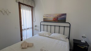 Ein Schlafzimmer mit Bett, einem Bild eines Bootes an der Wand, einem Nachttisch mit Lampe und einem Fenster mit Vorhängen.