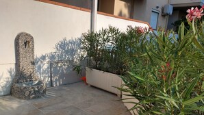Ein Steinfountain, Kübelpflanzen und eine geflieste Terrasse.