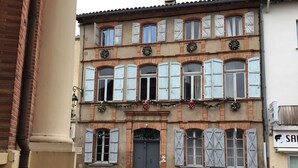 Un edificio de varios pisos con arquitectura tradicional, que presenta una entrada central con una puerta oscura, numerosas ventanas con contraventanas y decoraciones navideñas.