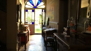 Un pasillo con suelo de baldosas que conduce a una puerta con un vitral. Se observan muebles de madera y un espejo a la derecha.