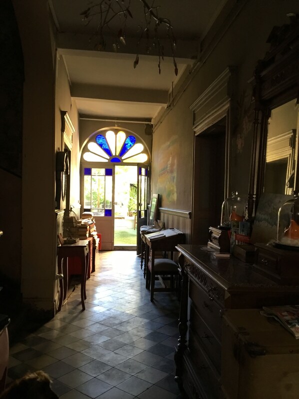 A hallway with a tiled floor leading to a door with a stained glass window. There are wooden furniture pieces and a mirror on the right side.