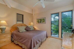 Un dormitorio con cama, lámparas de noche, ventilador de techo, ventana con persianas y un cuadro en la pared.