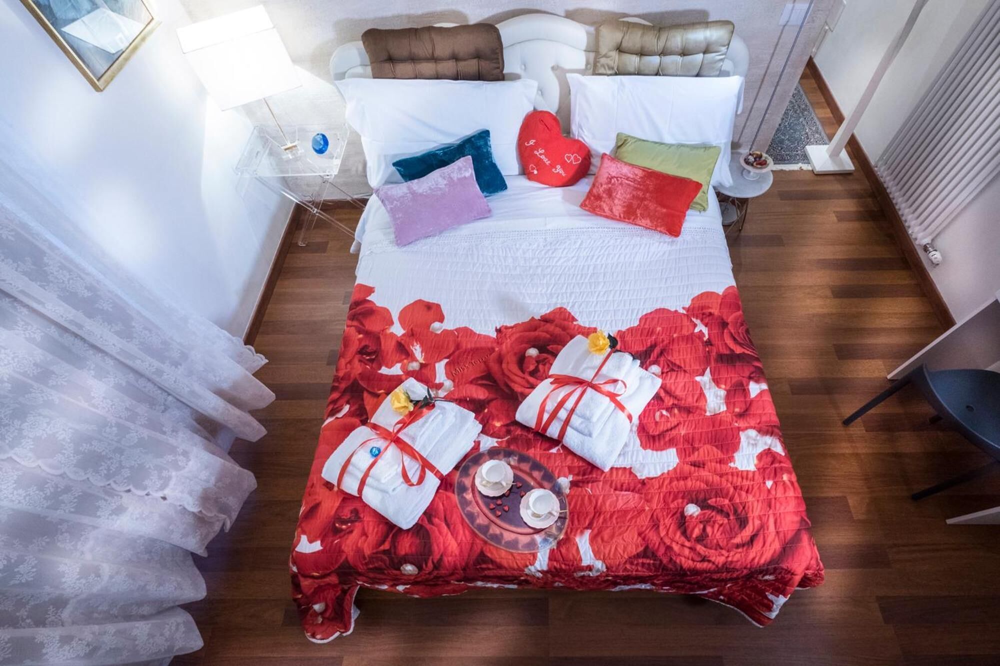 A bed with a red floral bedspread, multiple pillows, and a tray with cups and a teapot.