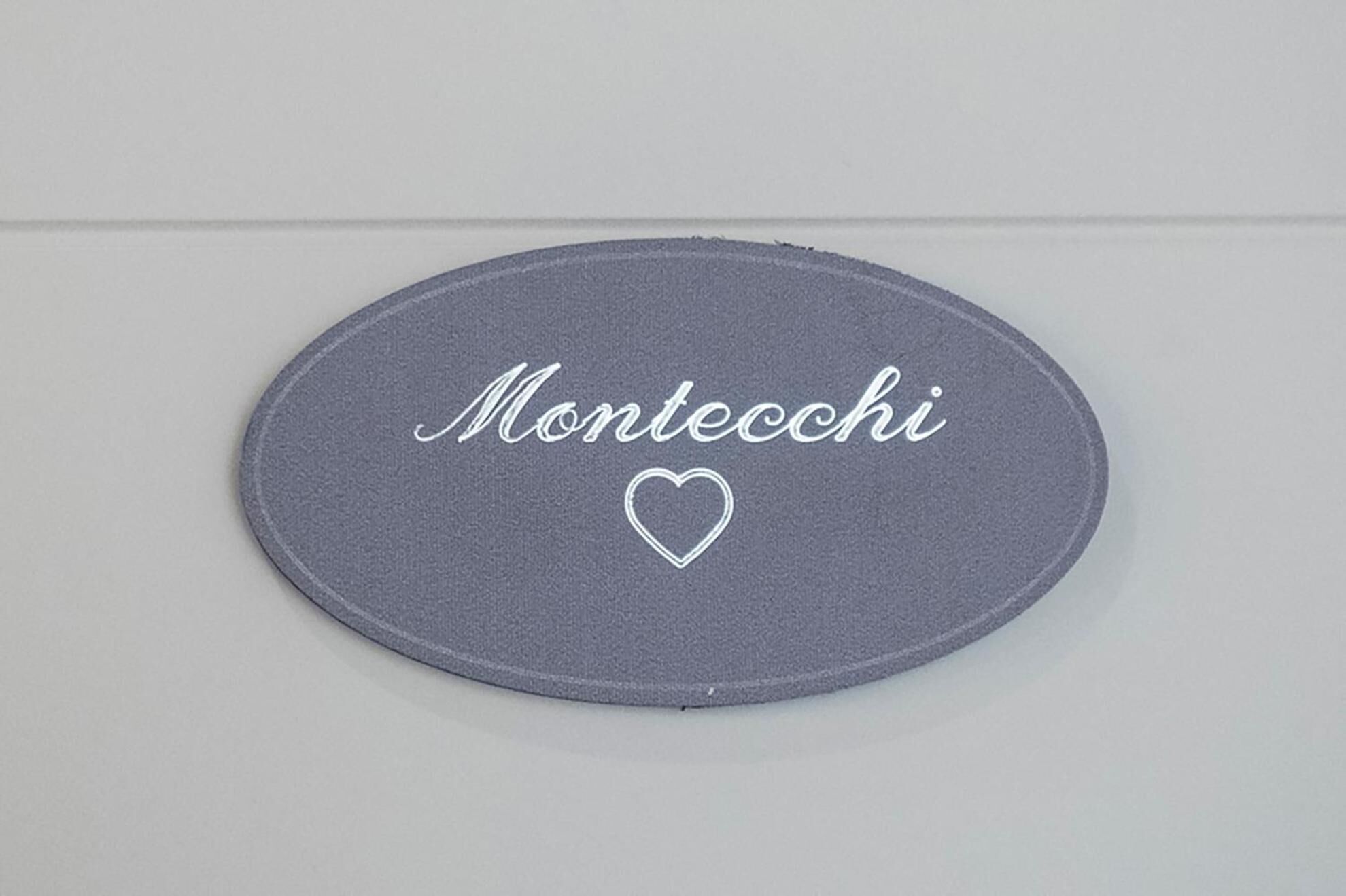 An oval-shaped fabric with the name "Montecchi" and a heart symbol embroidered on it.
