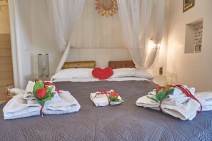 Een net opgemaakt bed met witte lakens, een rood hartkussen en handdoeken met rode rozen.