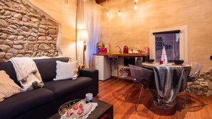 A cozy living room with a stone wall, a black sofa, a dining table with chairs, and a small kitchen area. - Abbraccio di Romeo e Giulietta (Verona)