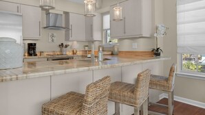 A kitchen with a marble countertop, wicker bar stools, pendant lighting, and a view of the outdoors. - ☀️Beachfront Complex-Top Floor-30A-Driftwood Cottage (Santa Rosa Beach)