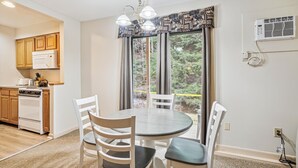 Un coin repas avec une table ronde et quatre chaises, une cuisine avec des meubles en bois et un four à micro-ondes, et une grande fenêtre avec des rideaux.