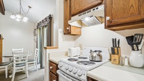 A compact kitchen with a white stove, a toaster, and a kettle on the countertop. Wooden cabinets and a chandelier are visible.